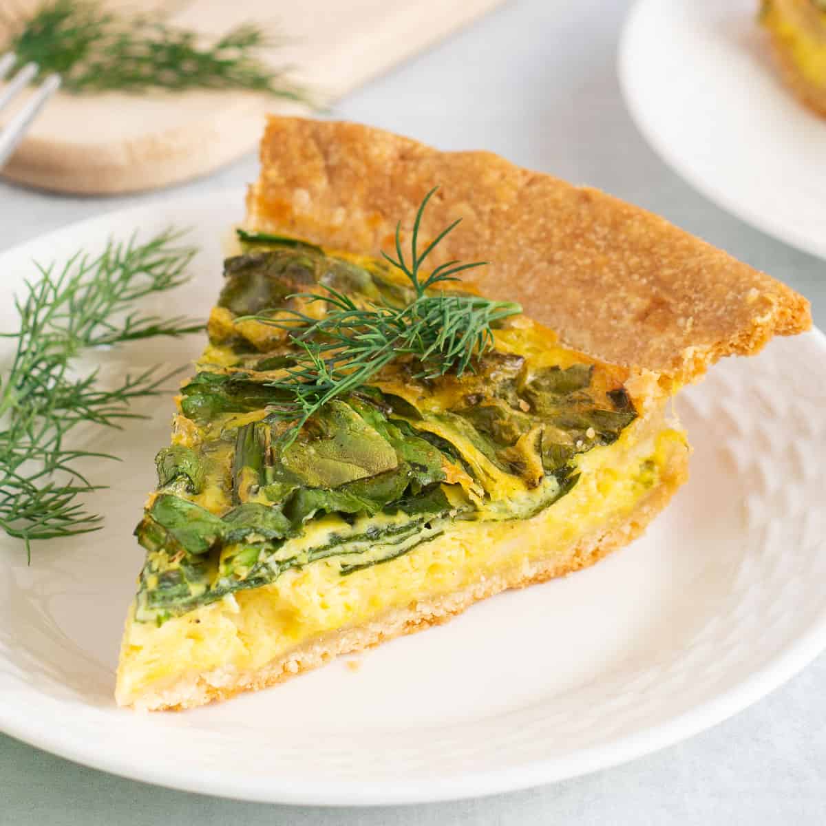 Slice of Just Egg quiche on white plate topped with fresh dill. 