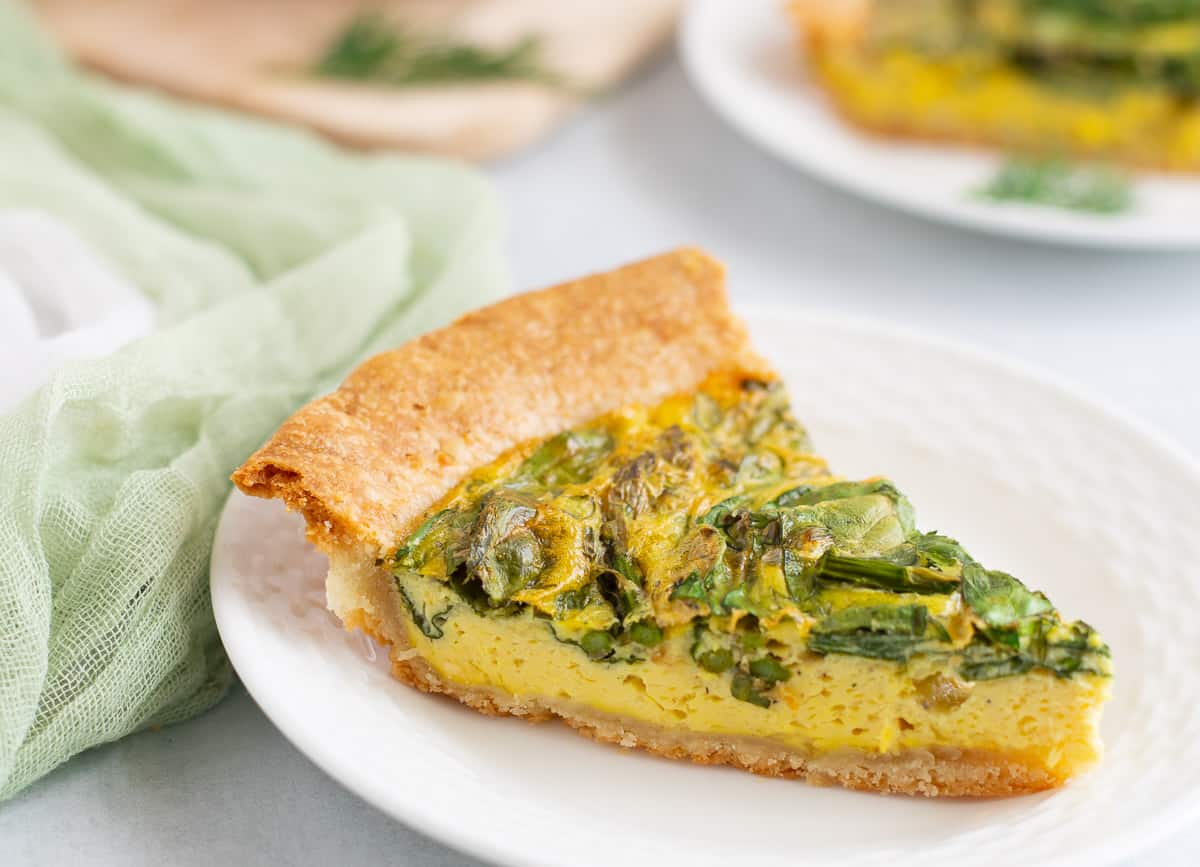 Slice of spinach and asparagus quiche on white plate. 