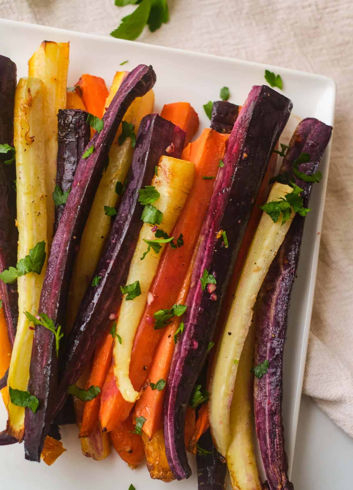 Roasted rainbow carrots on white square plate topped with fresh herbs. 