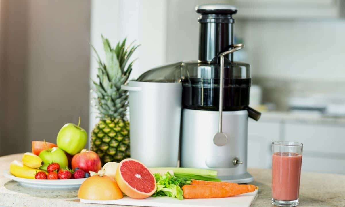 Juicer on counter with fruits and vegetables.