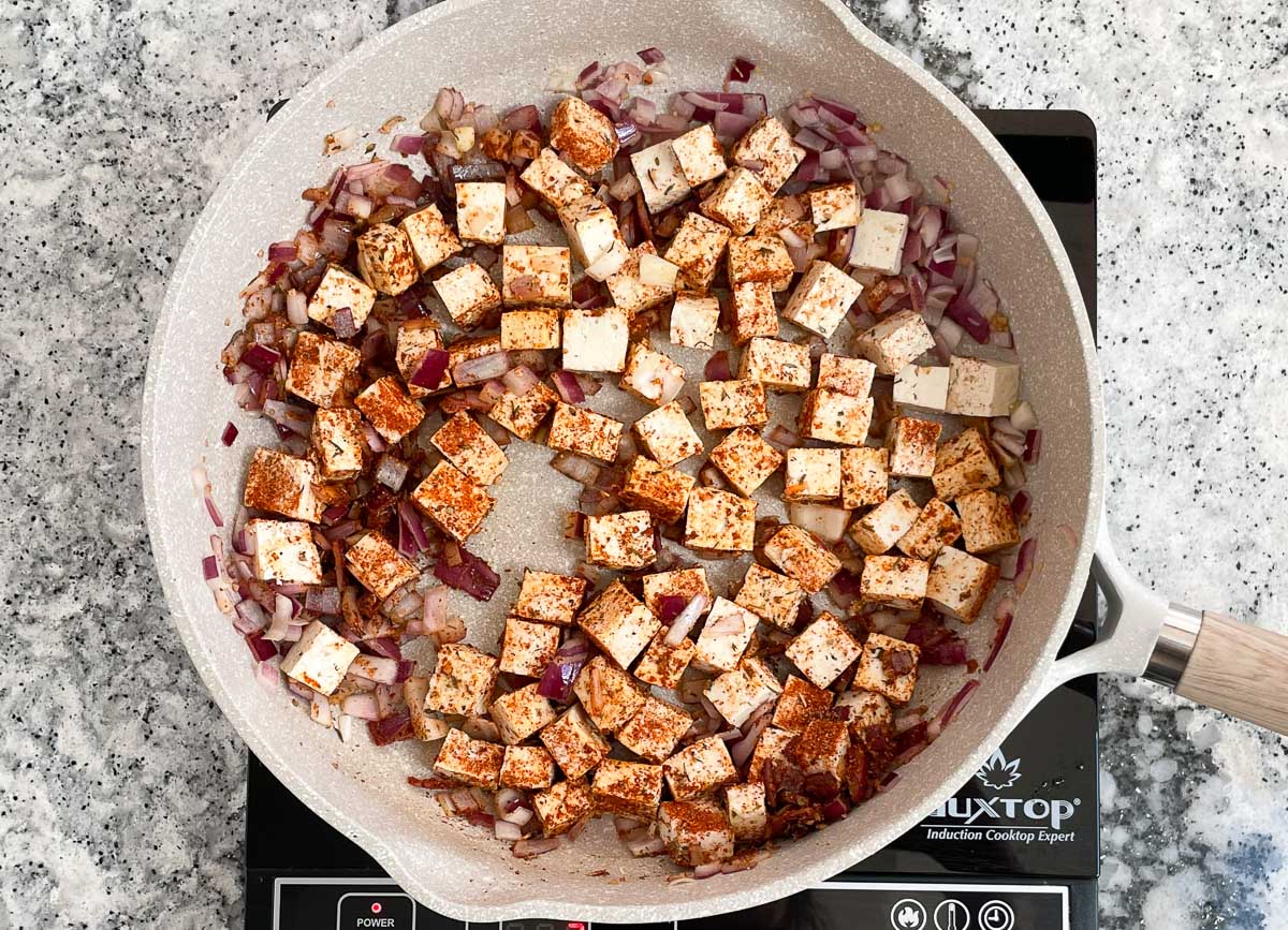 Tofu covered in spices in sauté pan with onions. 