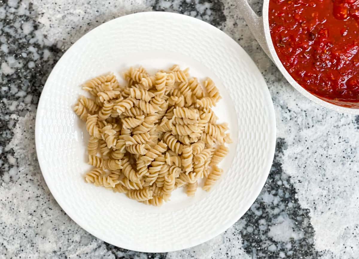 Pasta on white plate with a side or marinara sauce in pan. 