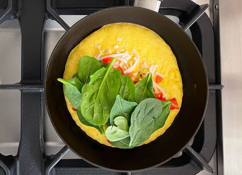 Adding spinach, tomatoes, and vegan mozzarella to omelette in pan. 