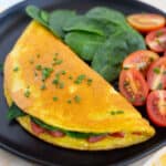 Just Egg omelette on black plate served with a side of spinach and sliced tomatoes.
