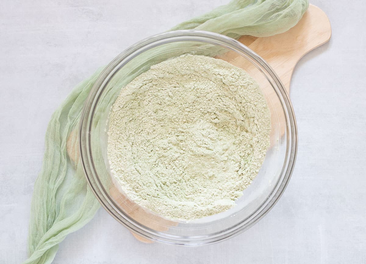 Flour and matcha powder whisked together in glass bowl. 