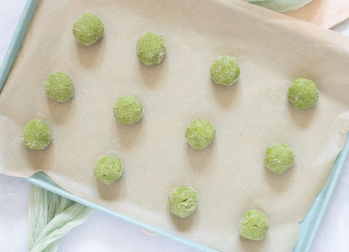 Balls of matcha cookie dough rolled in sugar and placed on baking sheet.
