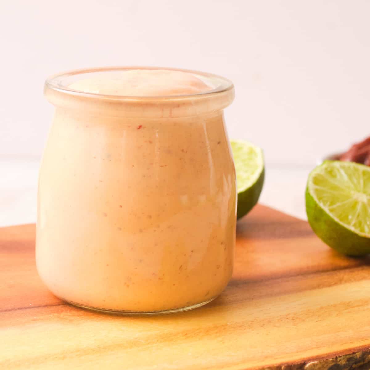 Vegan chipotle sauce in jar on wood cutting board with limes. 