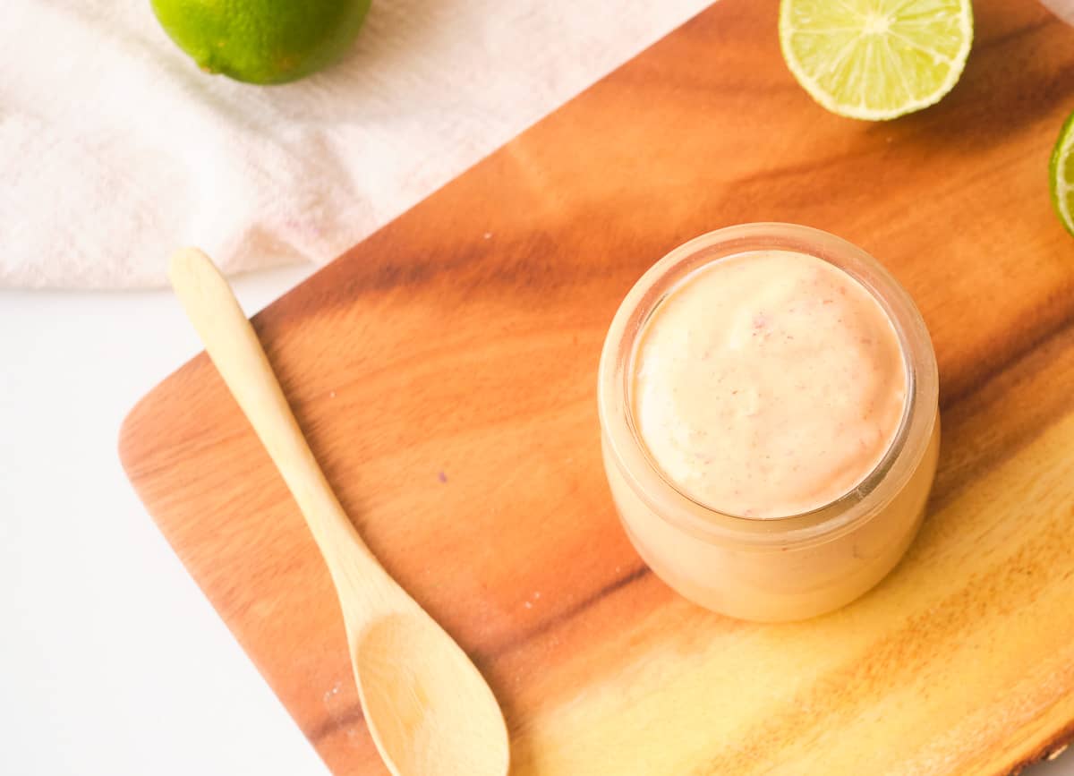 Creamy vegan chipotle sauce on wood cutting board with spoon and sliced limes. 