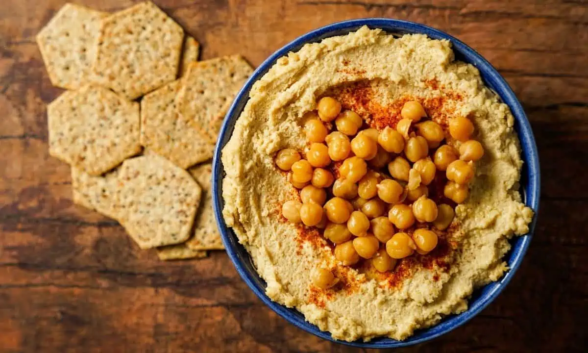 Hummus in a blue bowl with a side of crackers.