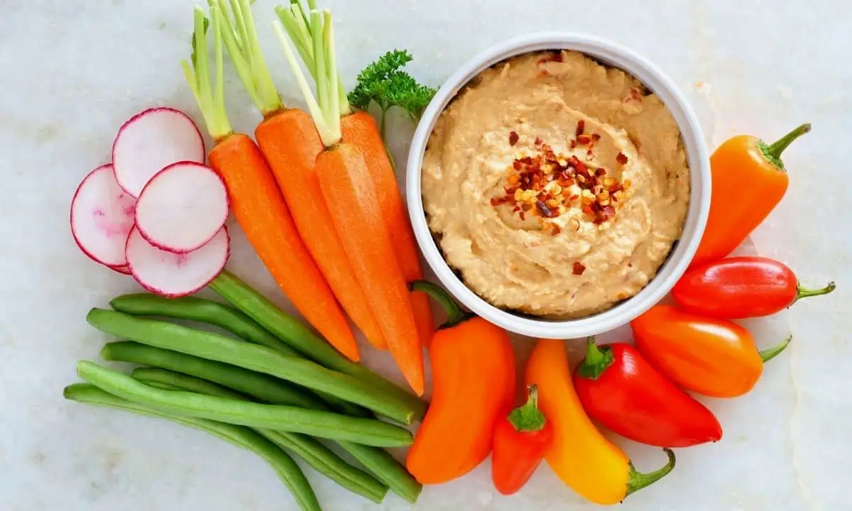 Hummus in a white bowl with vegetables for dipping. 