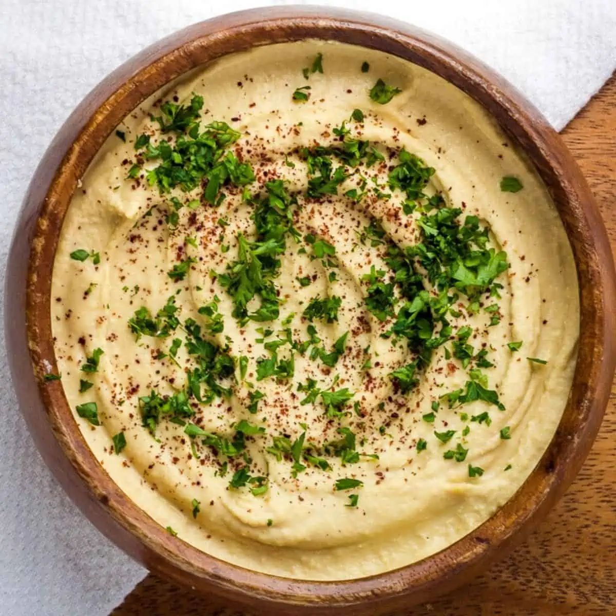 Hummus in a wood bowl, topped with parsley. 