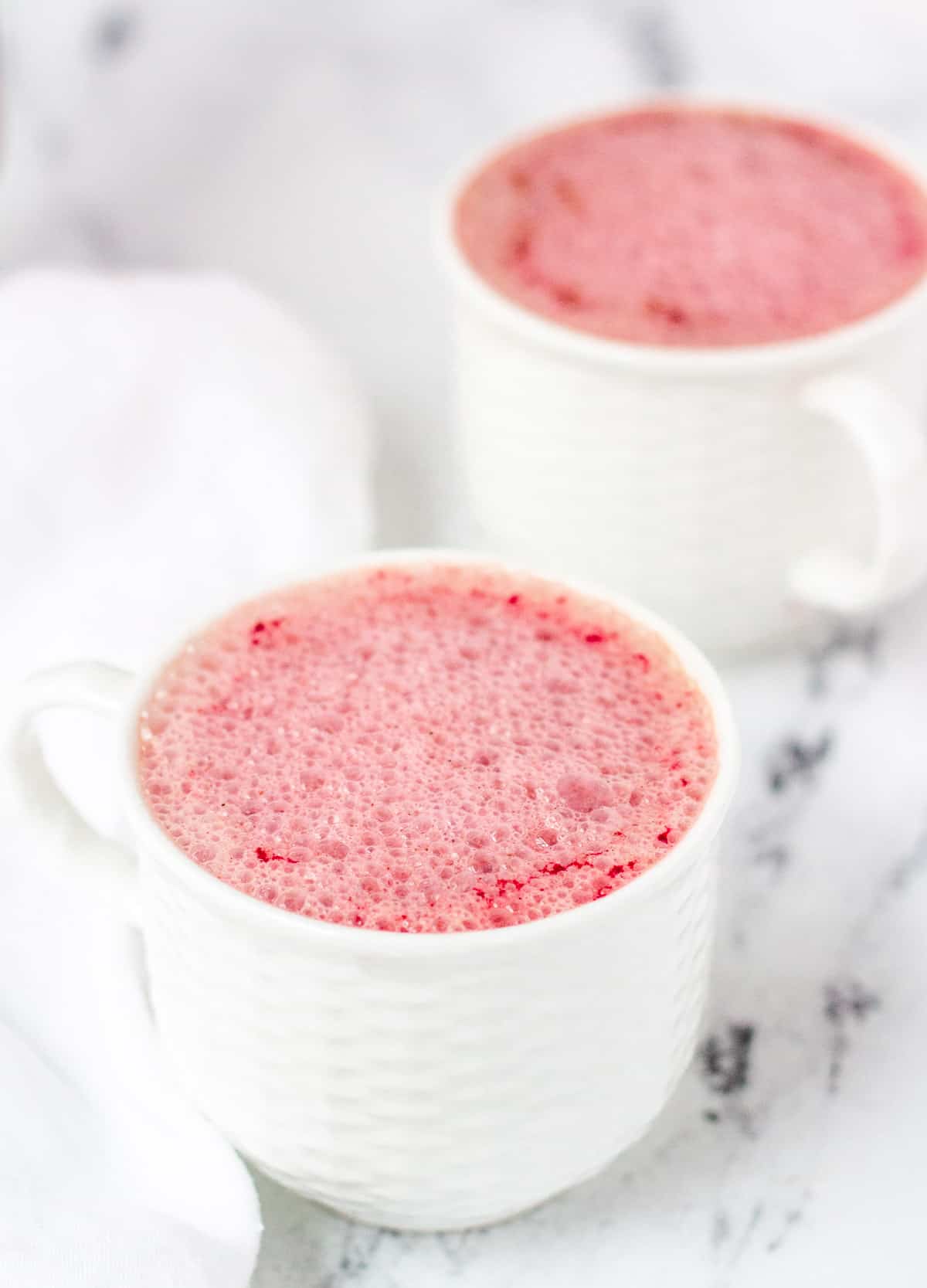 Two small white mugs filled with beet latte. 