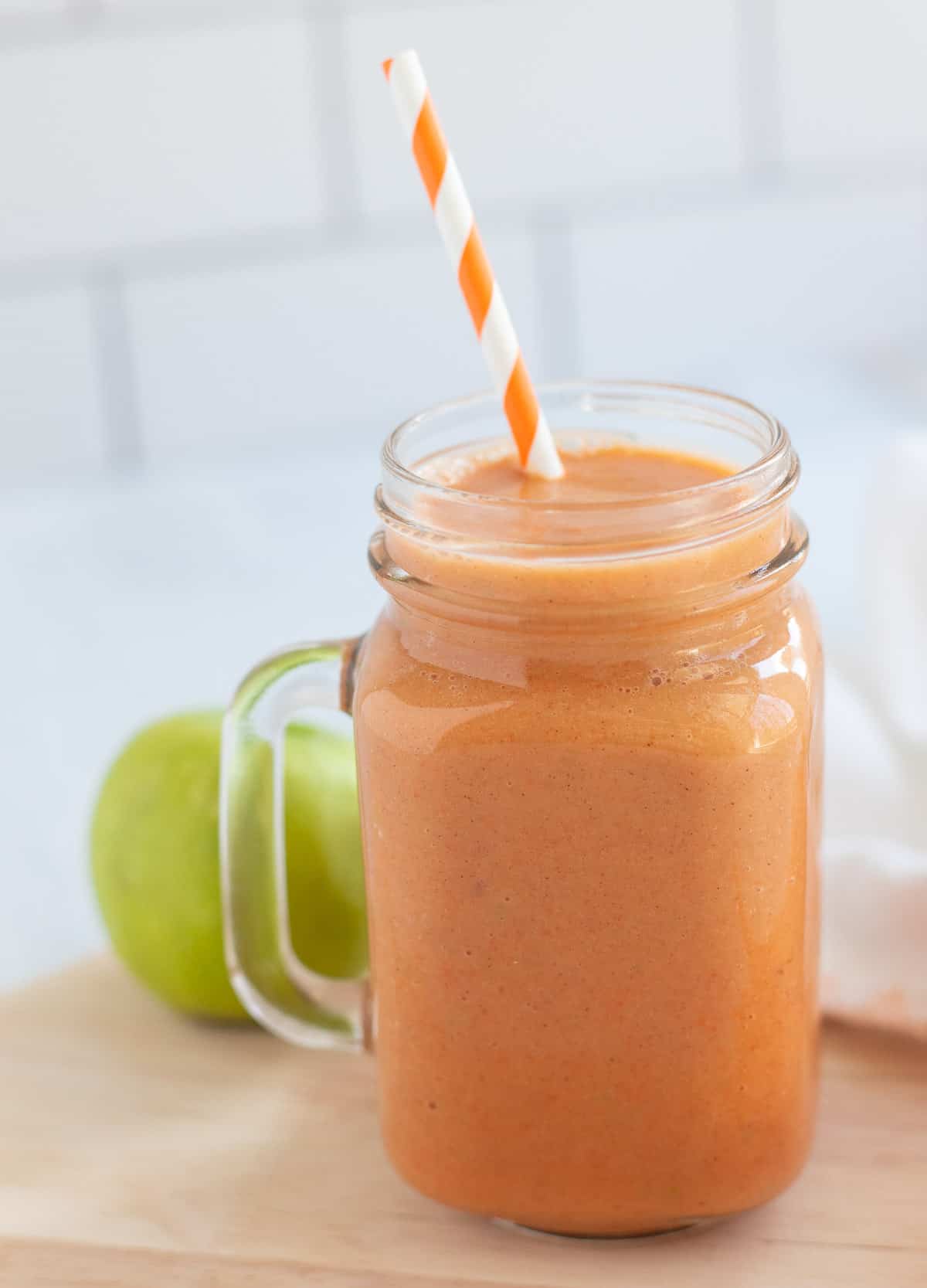 Apple carrot smoothie in glass mug with orange striped straw. 