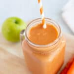 Apple carrot smoothie in glass mug with striped straw.