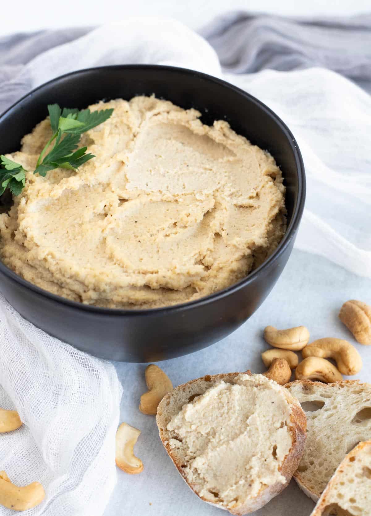 Cashew cheese in black bowl, served beside sliced bread.