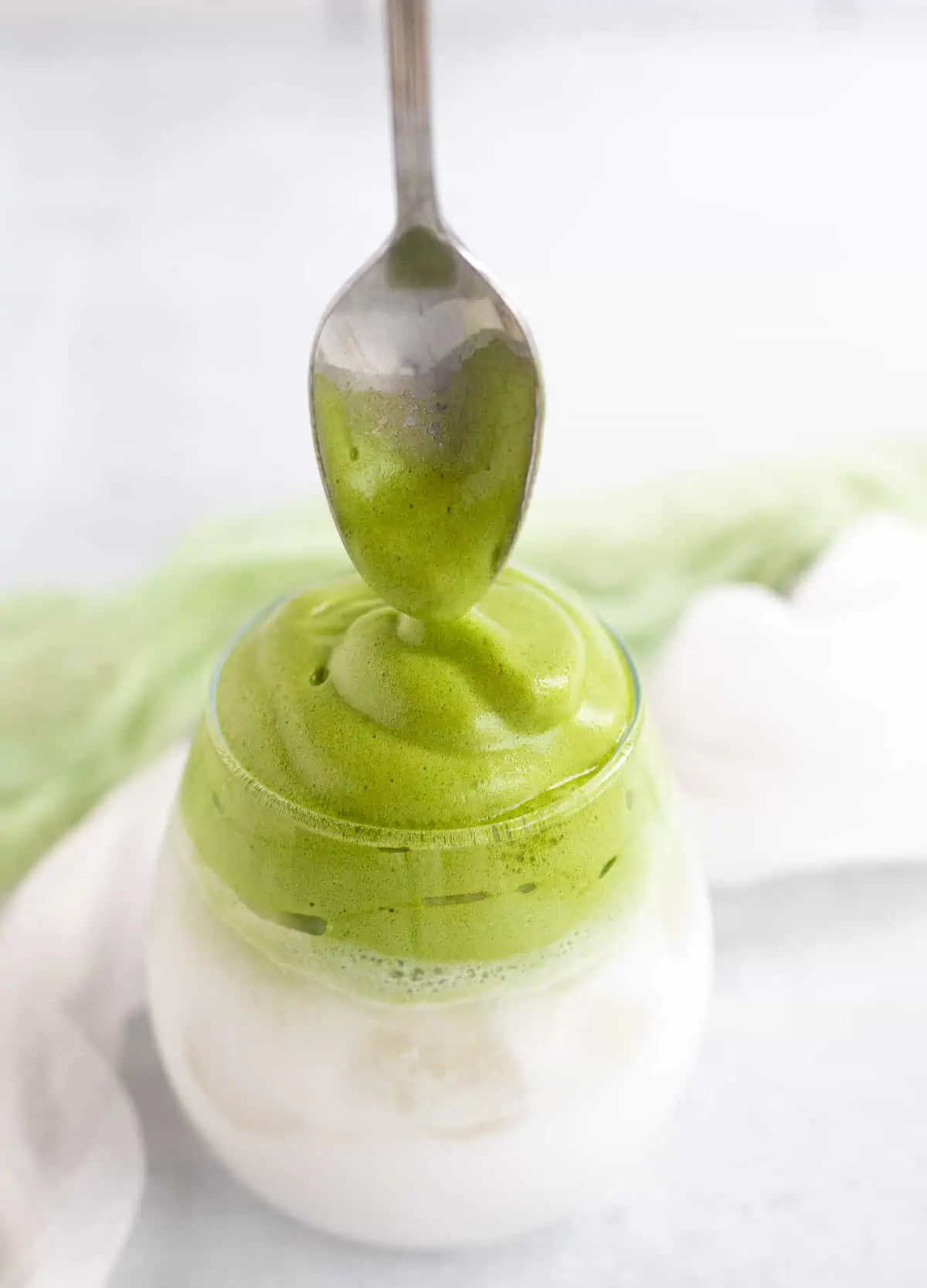 Spoon dipped into whipped matcha in glass.