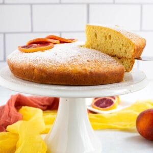 Slice of eggless orange cake lifted from whole cake on stand.