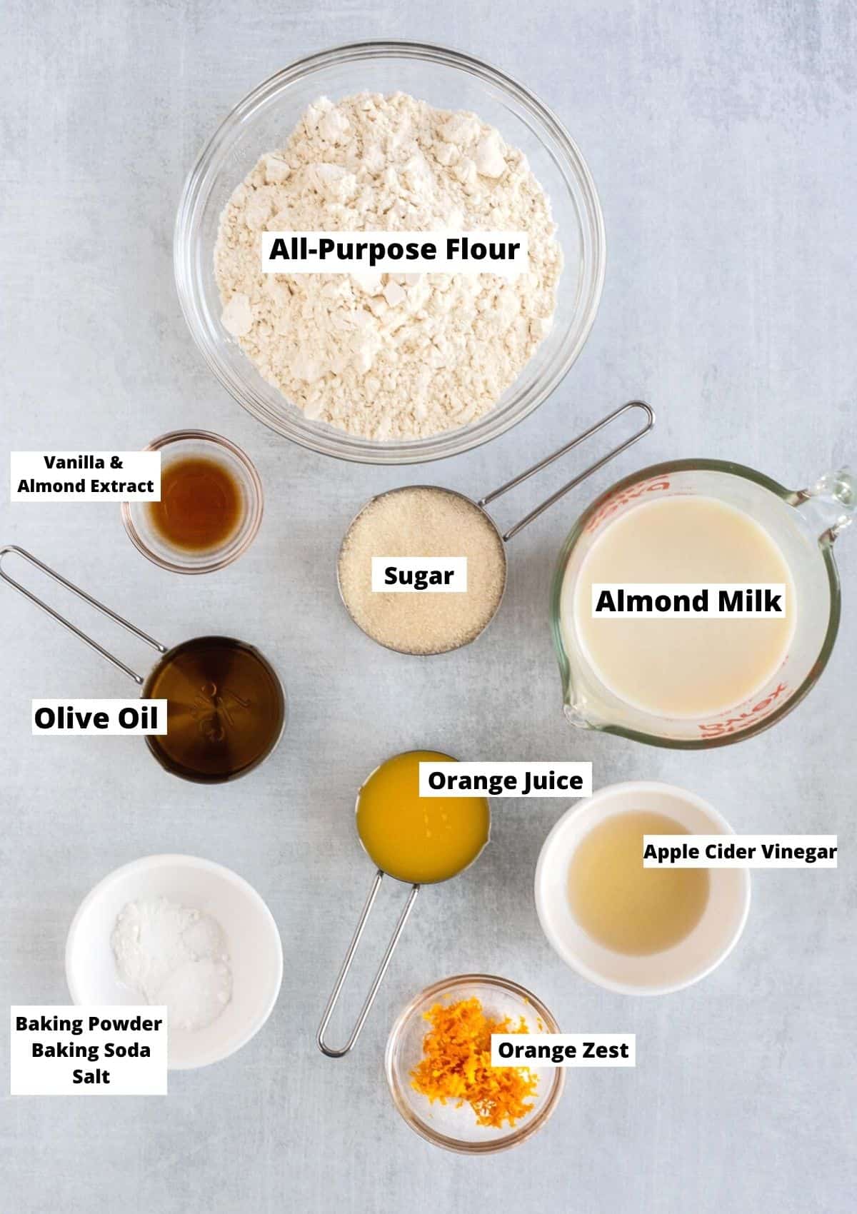 Ingredients for eggless orange cake: all-purpose flour, almond extract, vanilla extract, sugar, almond milk, olive oil, orange juice, sugar, apple cider vinegar, orange zest, baking powder, baking soda, salt. 