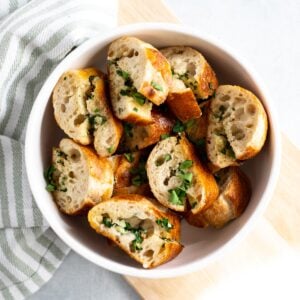 Sliced garlic bread with parsley in white bowl.