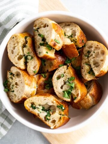 Sliced garlic bread with parsley in white bowl.