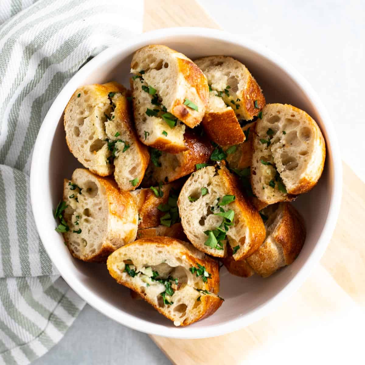 Sliced vegan garlic bread with parsley in white serving bowl. 