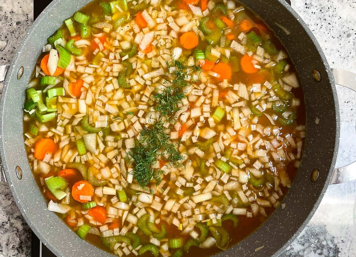 Vegetable broth and dill added to vegetables in pot. 