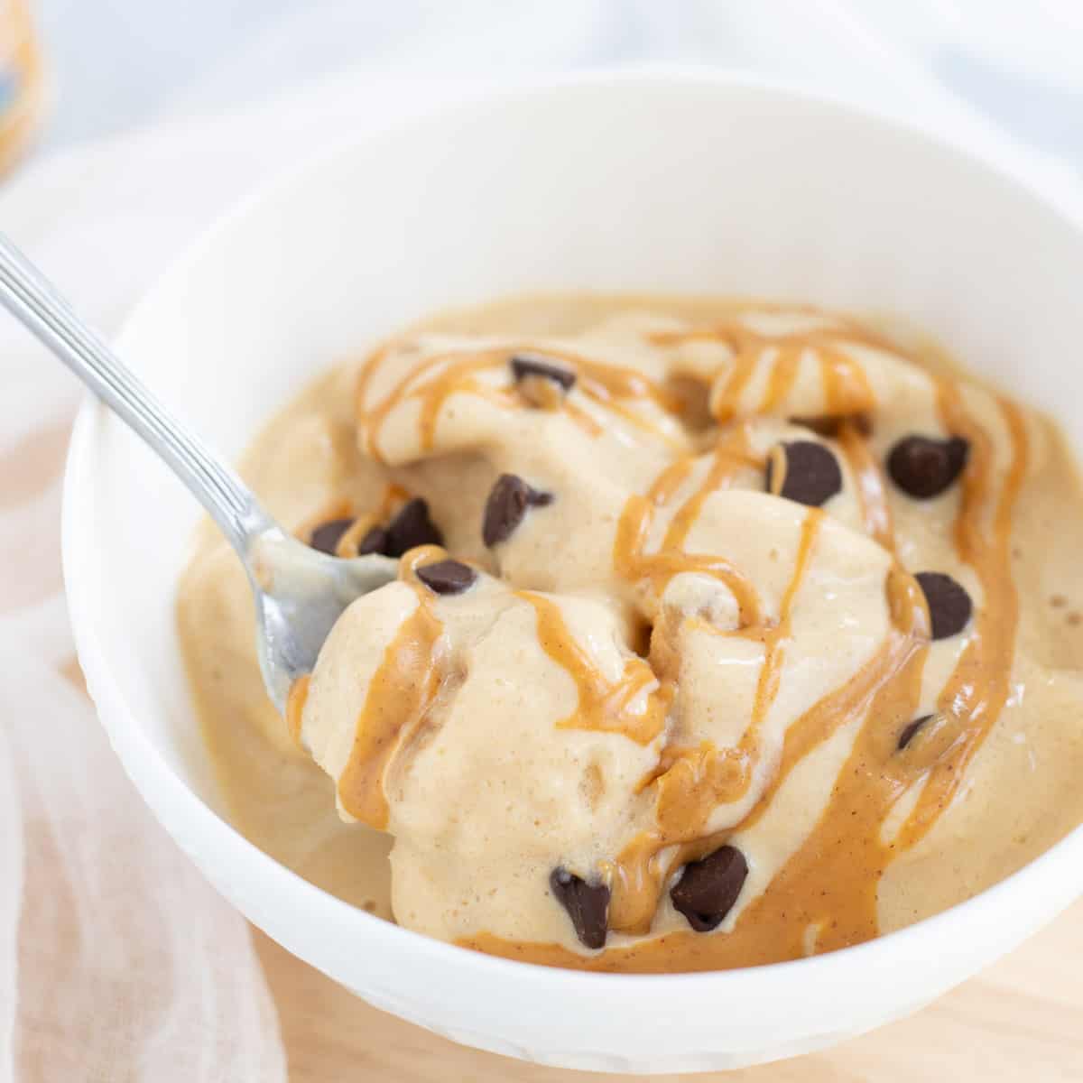 Protein fluff in white bowl with spoon, topped with drizzled peanut butter and chocolate chips. 