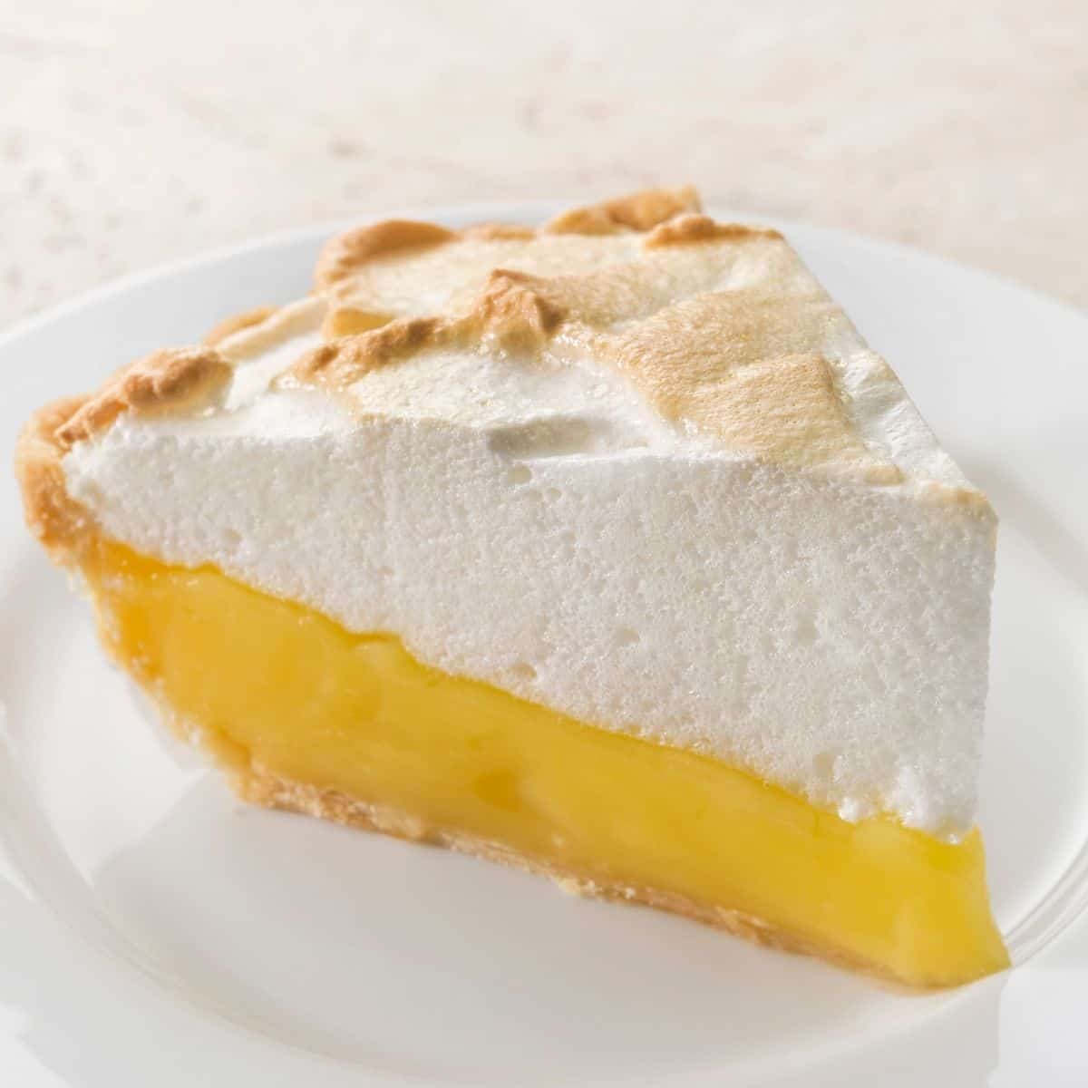 Slice of vegan lemon meringue pie on white plate.