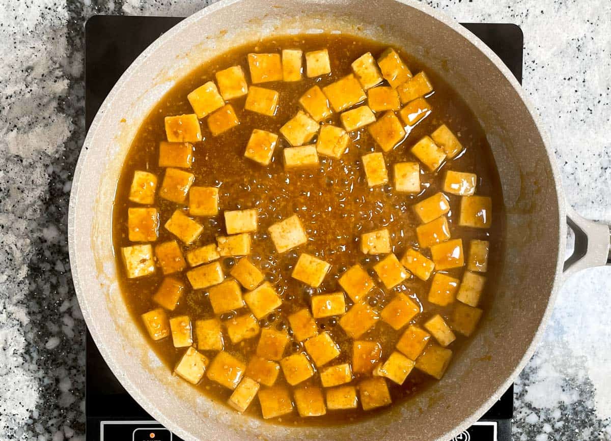 Tofu cubes covered in bubbling orange sauce in pan. 