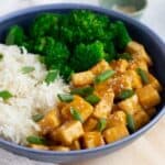 Vegan Orange Chicken in blue bowl served with white rice and steamed broccoli.