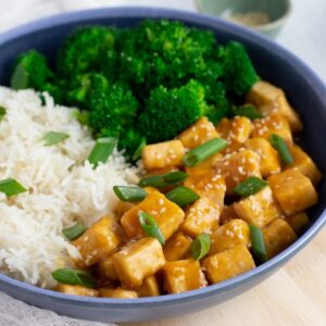 Vegan Orange Chicken in blue bowl served with white rice and steamed broccoli.