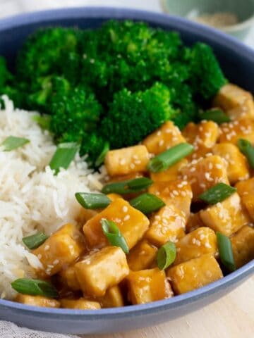 Vegan Orange Chicken in blue bowl served with white rice and steamed broccoli.