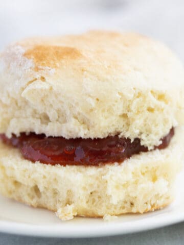 Scone on plate filled with strawberry jam.
