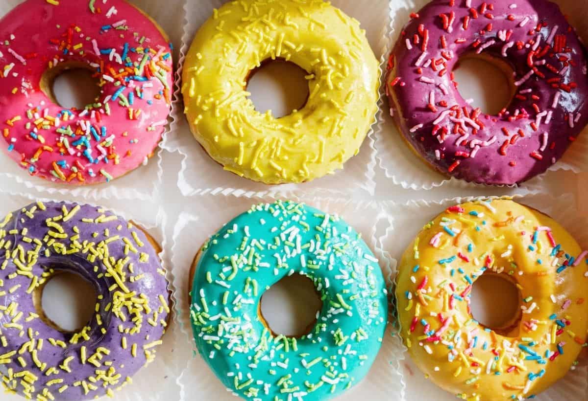 Overhead of colorful glazed donuts with sprinkles in box.