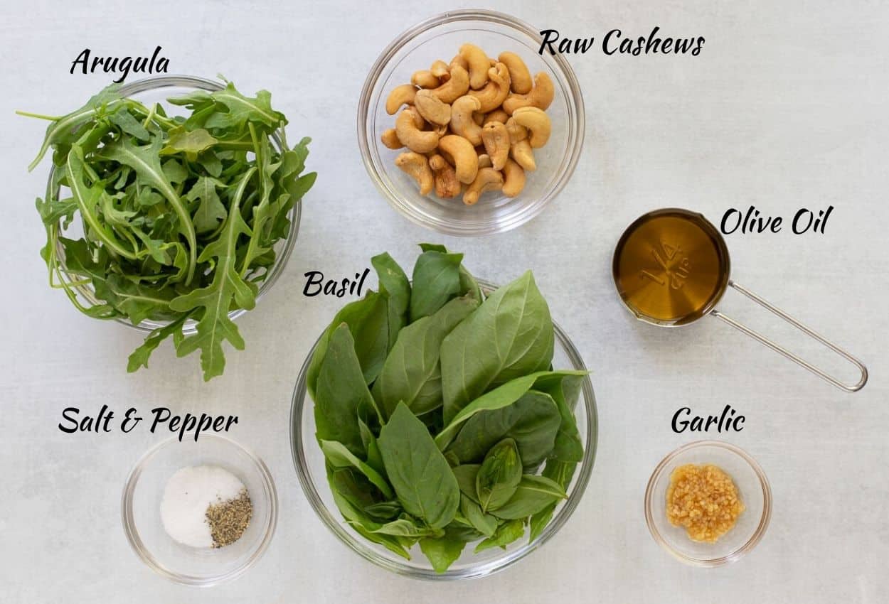 Cashew pesto ingredients: arugula, basil, salt, pepper, garlic, cashews, olive oil.