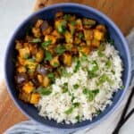 Eggplant and tofu in a blue bowl with rice topped with chopped cilantro.