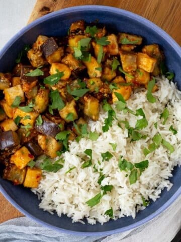 Eggplant and tofu in a blue bowl with rice topped with chopped cilantro.