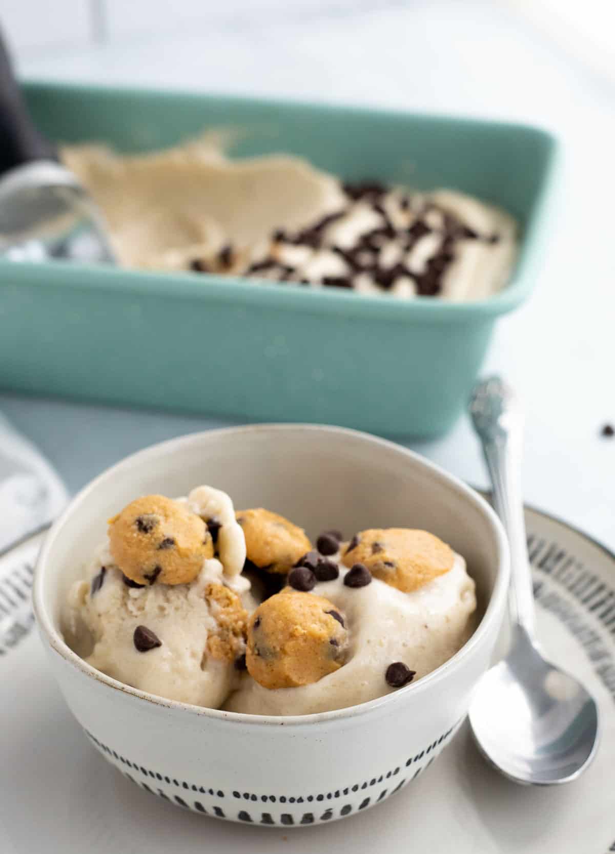 Cookie dough nice cream in small bowl on plate with spoon. 