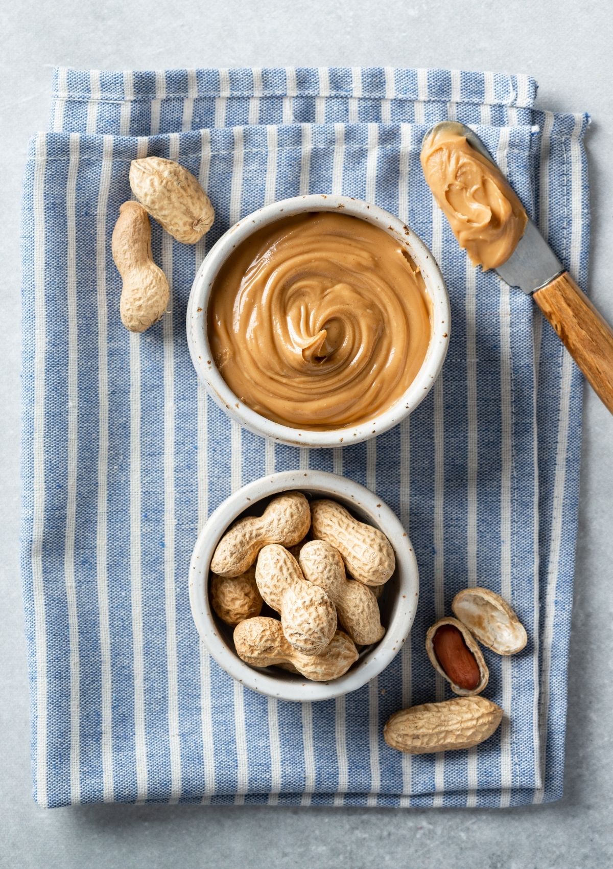 Peanut butter, peanuts, and knife with peanut butter on dish cloth. 
