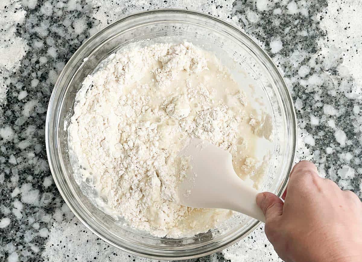 Folding almond milk into flour using spatula. 