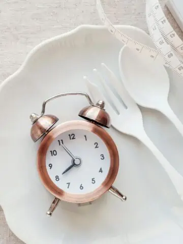 Clock on white plate with fork and spoon.