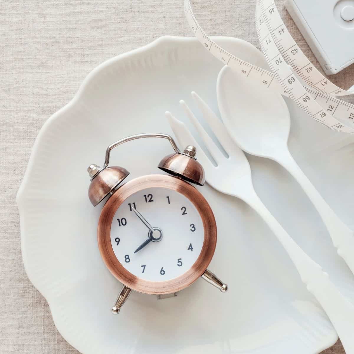 Clock on white plate with fork and spoon. 
