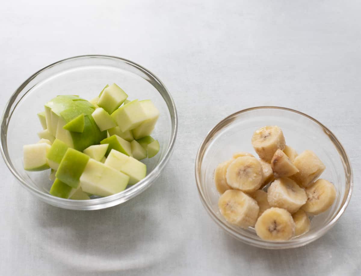 Chopped green apple, and chopped frozen banana in small glass bowls. 