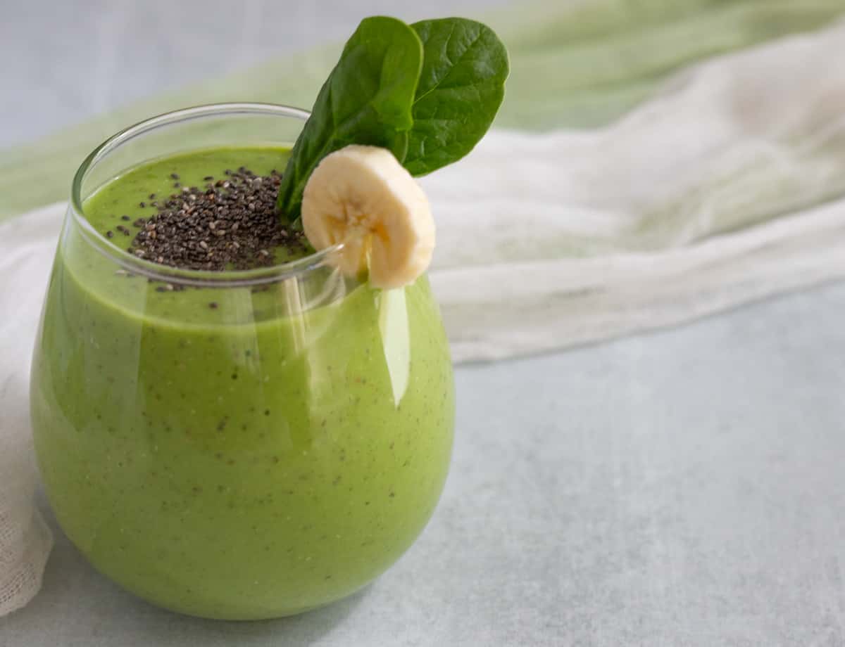 Spinach apple smoothie garnished with banana slice and spinach leaves.