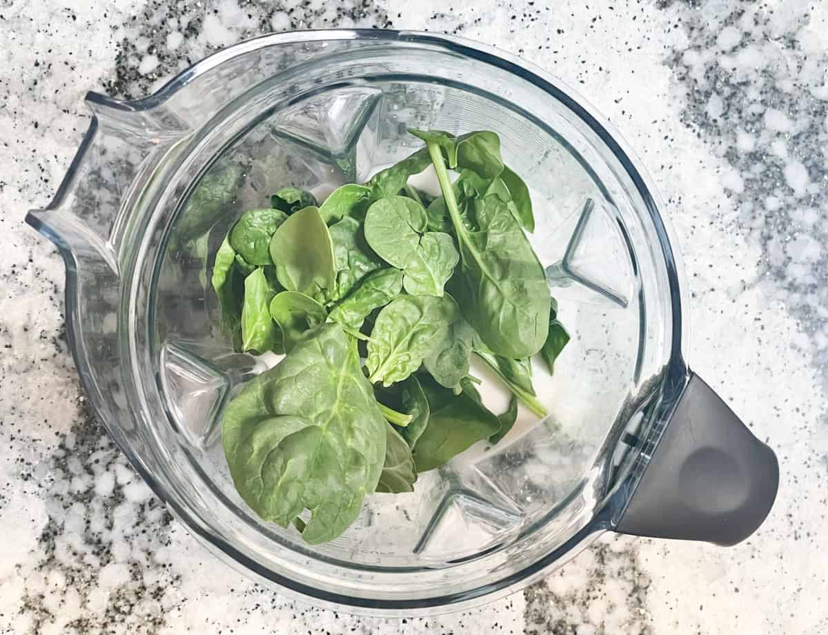 Spinach leaves added to blender with almond milk. 