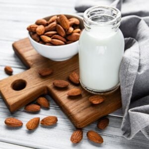 Almond milk in jug on cutting board surrounded by raw almonds.