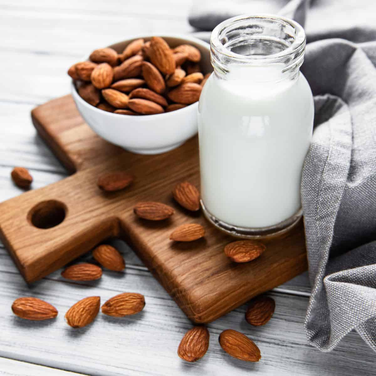 Almond milk in jug on cutting board with raw almonds. 