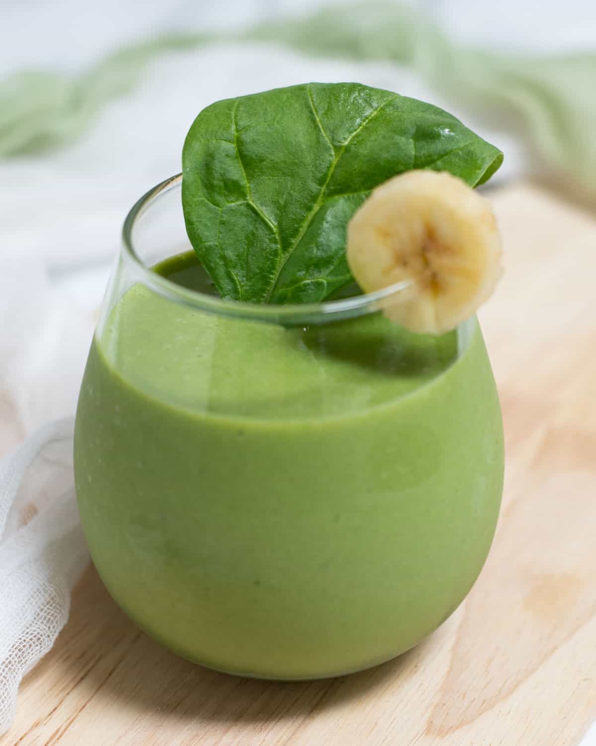 Glass filled with green smoothie topped with banana and spinach leaf. 
