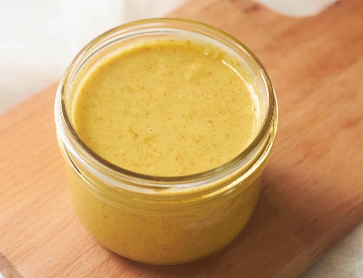 Vegan Honey Mustard in small jar on top of cutting board.