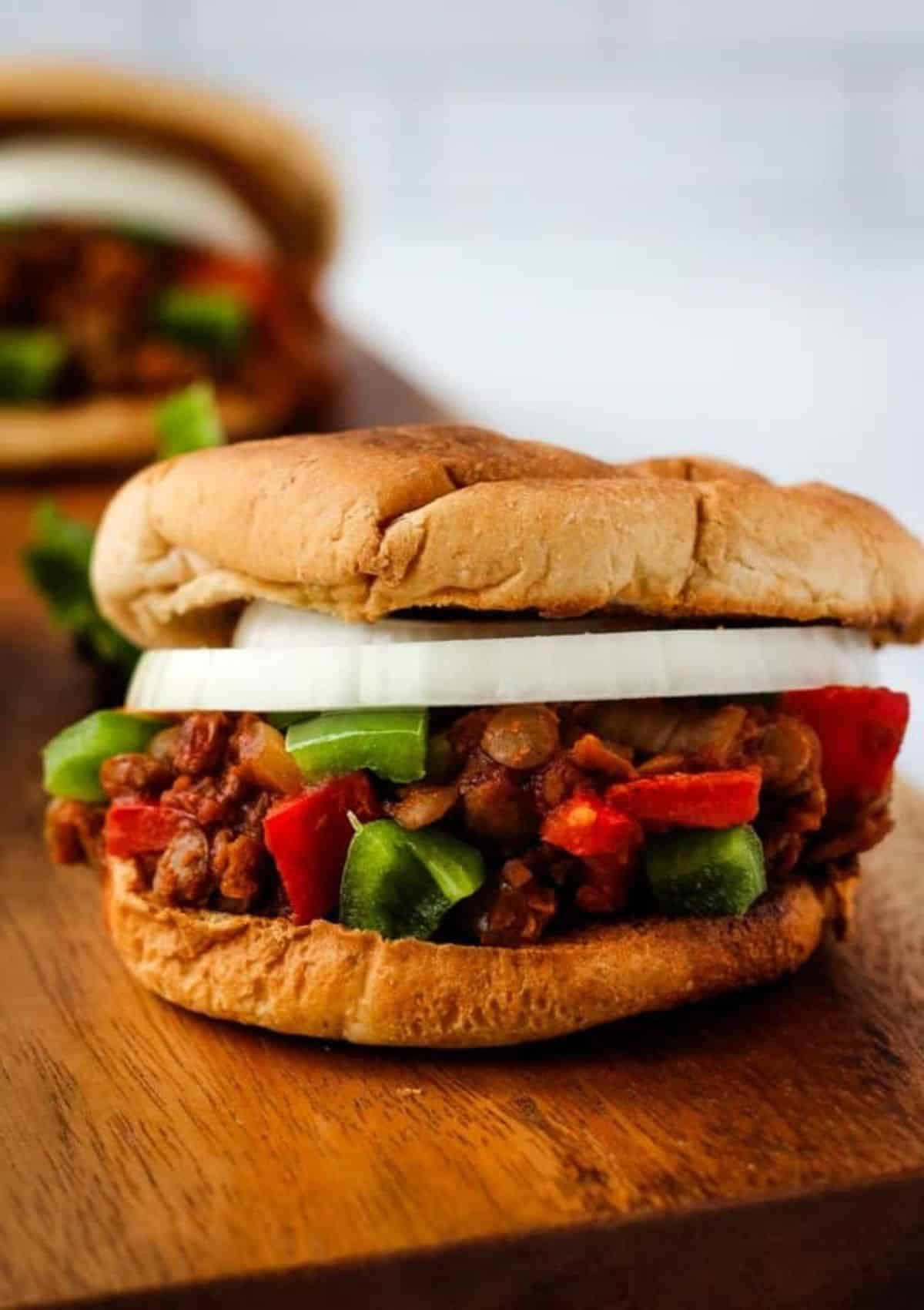 Close-up of a vegan sloppy Joe with onion sandwich sitting on wood table.